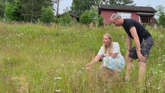En kvinne og en mann i en blomstereng med en rød hytte i bakgrunnen.