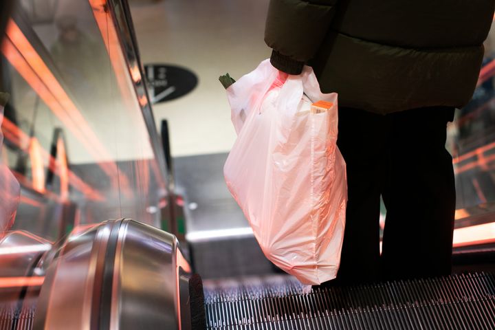 Person på rulletrapp med plastpose i hånden.