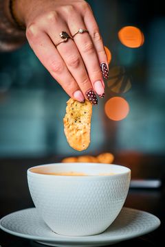 En kvinnelig hånd dypper et stykke brød i en bolle med hummersuppe.