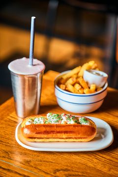 En lobster roll på en tallerken med en shake og pommes frites i bakgrunnen.
