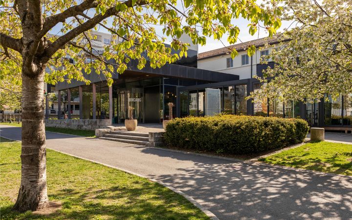 Kanonhallen på Løren med store vinduer omgitt av blomstrende trær og en parkarealer.