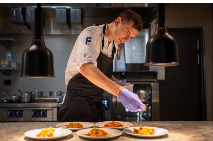 En kokk i et restaurantkjøkken legger siste hånd på en serie ferdige retter.