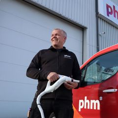 Vidar Andreassen, daglig leder i PHM Skadedyrkontroll står foran en PHM Skadedyrkontroll-bil og smiler, mens han holder en sprayenhet.