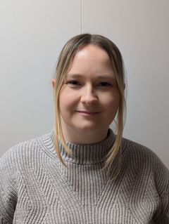 Det er et portrett av en kvinne med langt hår, kledd i en grå genser.