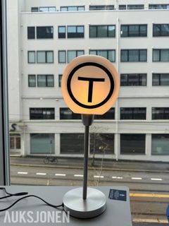Dette er en helt unik sjanse til å sikre deg et stykke Oslo- og designhistorie. Denne eksklusive bordlampen er en utformet miniatyrutgave av det klassiske T-baneskiltet som markerer nedgangene til T-banestasjonene i hovedstaden.