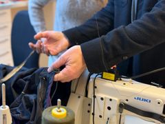 Person som arbeider med å reparere en Gore-Tex-jakke ved en symaskin.