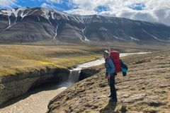 Person i friluftsklær står ved en elv i et fjellandskap på Svalbard.