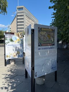 Utstilling med plakater om tidlig utforskning av Antarktis, plassert utendørs med en bygning og trær i bakgrunnen.