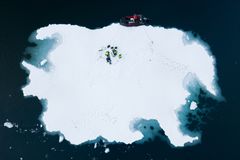 Dronefoto av tre personer som jobber på en isflak i Antarktis, med en rød båt fortøyd ved kanten.
