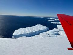 Et rødt flyvinge overflyr store isflak i et havlandskap.