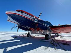 Et modernisert propellfly fra 1940-tallet står parkert på snøen under klar blå himmel.
