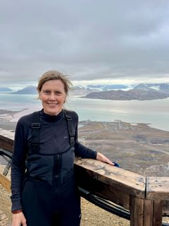 Person står foran en fjord og snøkledde fjell.