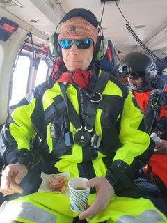 Mann i helikopter, iført sikkerhetsdrakt, holder en kopp.