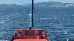 Et seilbrett krysser foran et lasteskip i Oslofjorden.