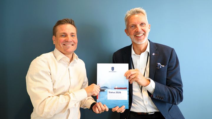 To personer smiler og holder et hefte med tittelen "Status 2026".