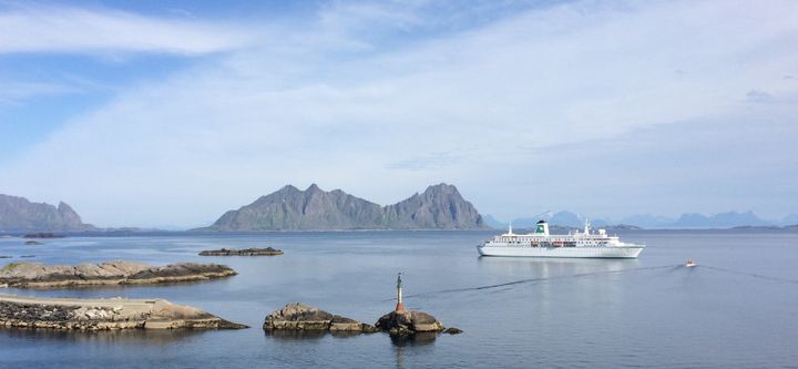 Et cruiseship seiler nær klipper med fjell i bakgrunnen i Svolvær, Lofoten.