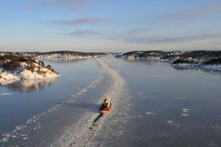 En isbryter som baner seg vei gjennom et islagt fjordlandskap med snødekte øyer i bakgrunnen.