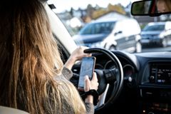 Bilde av kvinne som sitter i førersetet på en bil og holder en mobiltelefon i hånden