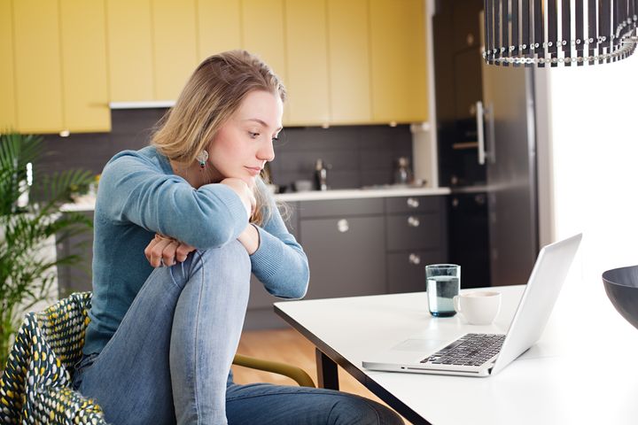 Ung kvinne sitter ved et spisebord og ser på en PC. Foto.
