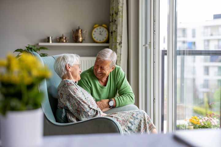 Et eldre par sitter i en stue, snakker sammen og ler. Foto.
