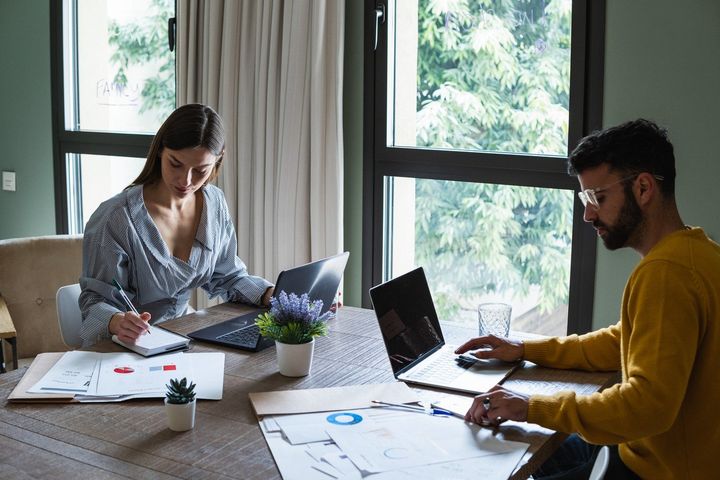 To studenter sitter ved et bord med PC og papirer. Foto.