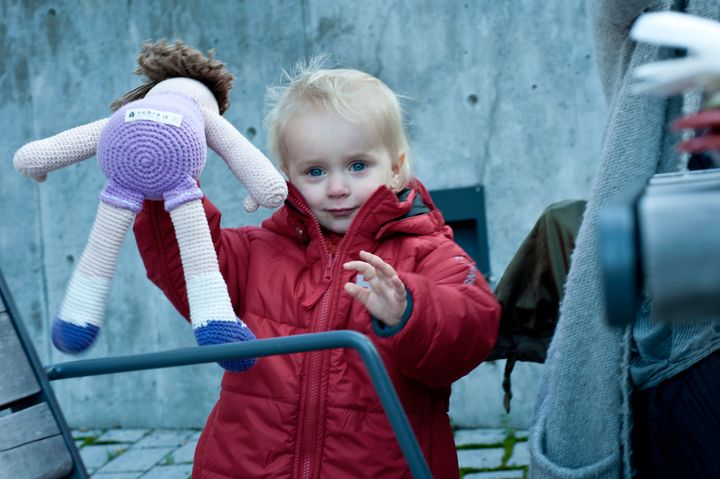 Rødkledt barn som holder opp en dukke.
