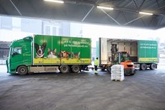 Lastetruck laster varer på en grønn og gul Felleskjøpet-lastebil med henger.