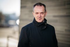 Kjetil Houg i mørk jakke står utendørs foran en murvegg.