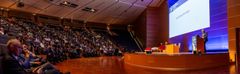 Bilde av en stor konferansesal med mange mennesker som sitter i publikum. En person holder en presentasjon på scenen under European Robotics Forum 2024.
