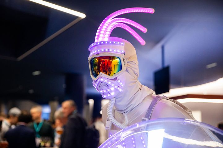 A person in a futuristic outfit with LED lights and mirrored goggles at the European Robotics Forum 2025.