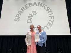 To kvinner holder et papirbevis mellom seg. I bakgrunnen står det "Sparebankstiftelsen DNB".