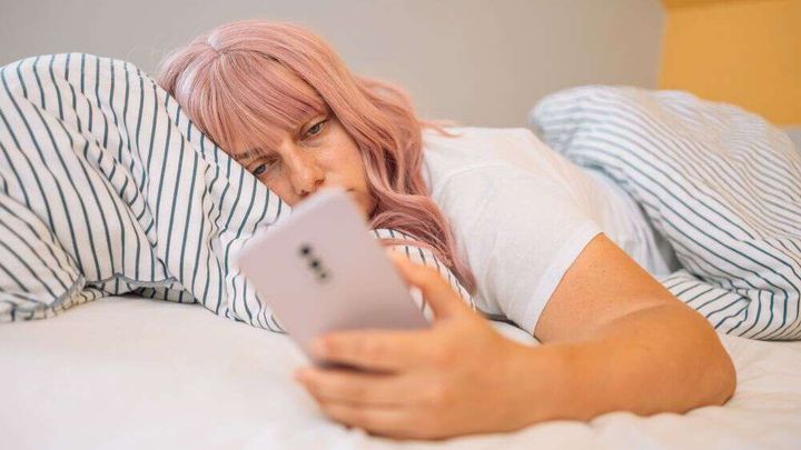 trøtt dame ser på mobil i sengen