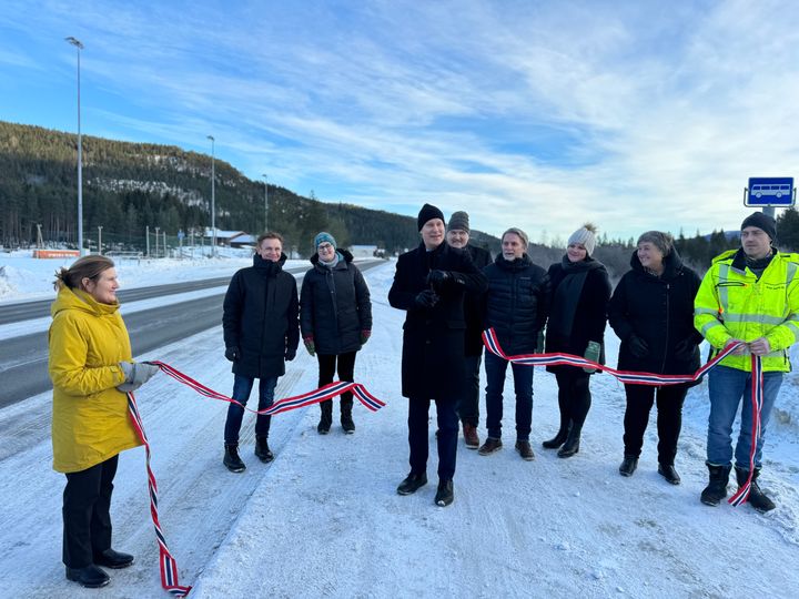 Samferdselsministeren klipper snora for ferdigstilling av utbetringsprosjektet på E16 mellom Fagernes og Øylo i Valdres. De står utendørs langs vegen i snølandskap.