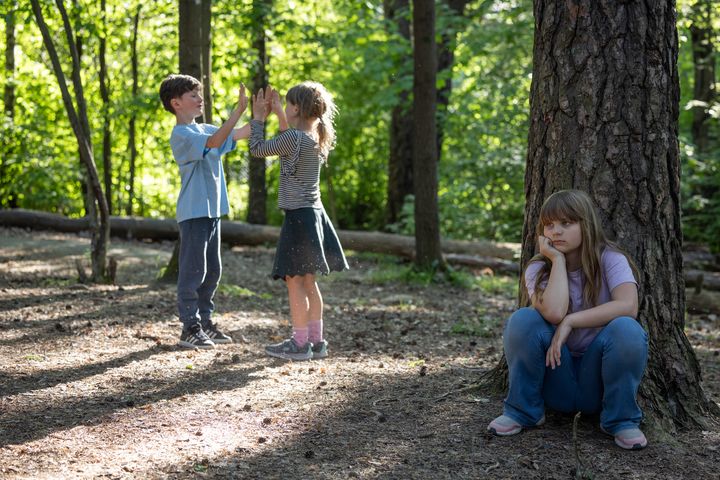 Barn leker i skogen - ei jente sitter alene