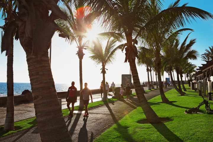 Fornøyde turister som spaserer langs stranden på Gran Canaria i solnedgangen.