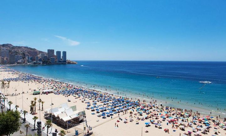 En strand full av mennesker og parasoler på Benidorm i Spania.