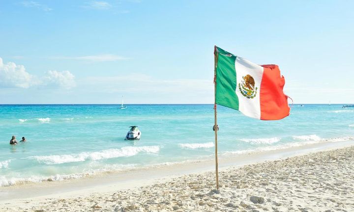 Vakker strand med et meksikansk flagg plantet i den hvite sanden.