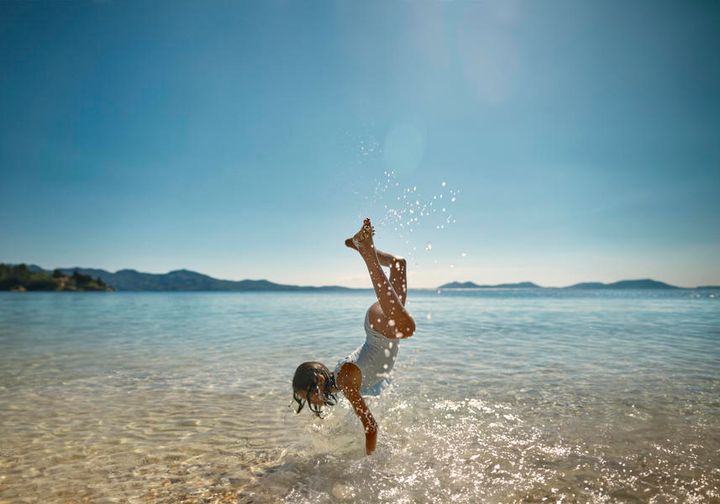 Liten jente som står på henda på en strand på Mallorca.