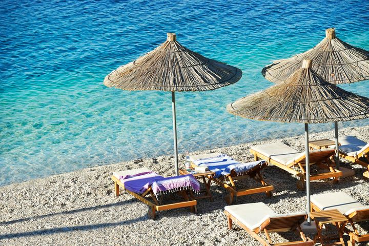 Strand i Saranda i Albania med to solsenger og blåt hav.
