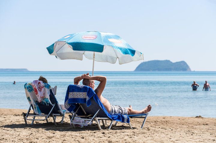 Et par som ligger på hver sin solseng på en strand i Zakynthos Hellas.