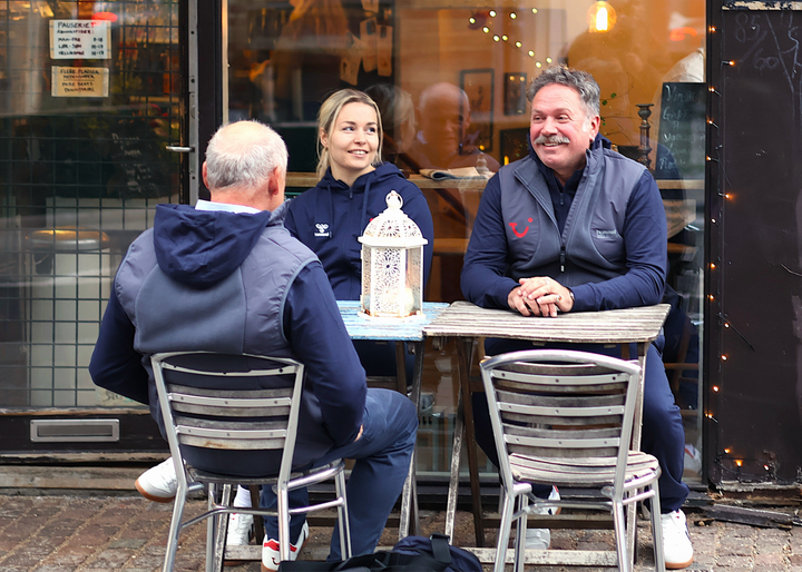 Tre personer på en utservering som har på seg klær med Hummel og TUI-logo.