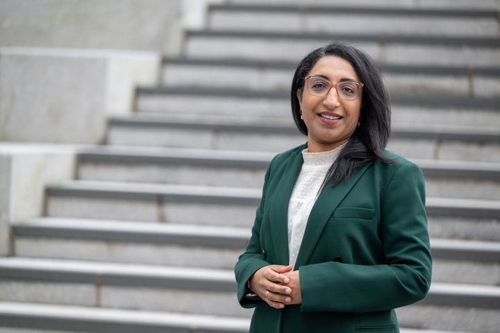 En person står foran en trapp ikledd grønn blazer og briller.