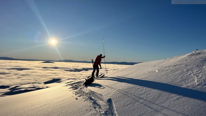 Bildet viser en som gjør undersøkelser av snøen. Tåka ligger nede i dalen.