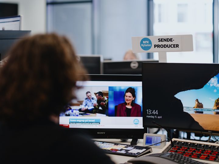 En ansatt i NRK med to dataskjermer foran seg. Den ene skjermen viser skjermspareren fra Microsoft.