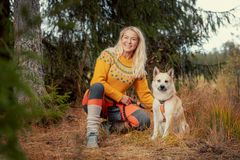 En kvinne kledd i fargerike klær sitter i skogen med en hvit hund ved sin side.