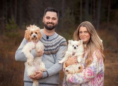 En mann og en kvinne bærer på hver sin hund stående i en skog.