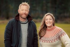 En mann og en kvinne som smiler, kledd i strikkegensere, stående utendørs.