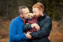 To menn i en skog klemmer en liten hund.