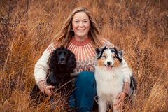 En kvinne sitter ute i naturen med to hunder ved sin side.