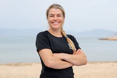 Hedvig Wessel smiler med armene i kors på en strand, iført svart Mesternes mester-drakt med hav og fjell i bakgrunnen.